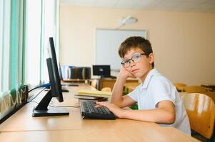 Teenage boy smiling while using computer at desk in classroom photo
