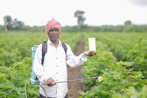 Indian farmer working on farm field, spraying fertilizer on soil and plants. photo