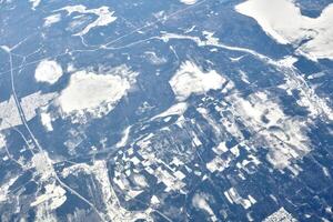 Aerial view from airplane window over clouds top to snow covered rivers, fields and roads photo
