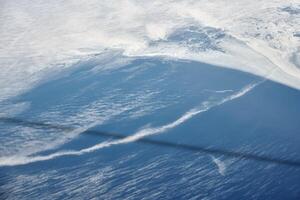Aerial view from airplane window over clouds to frozen sea with north steam gas pipeline underwater photo