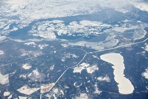 Aerial view from airplane window over clouds top to snow covered rivers, fields and roads photo