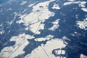 Aerial view from airplane window over clouds top to snow covered rivers, fields and roads photo