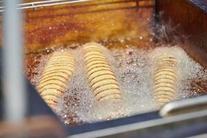 Cooking spiral fried potato in boiling oil, rich in fat and calories fast food, unhealthy delicious photo