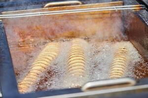 Cooking spiral fried potato in boiling oil, rich in fat and calories fast food, unhealthy delicious photo
