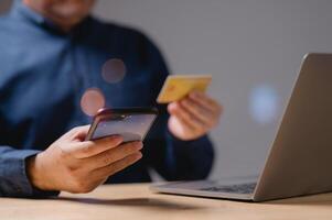 Transactions convenience and modern technology concept. A man is using his phone and laptop to pay for something. He is holding a credit card in one hand and a phone in the other. photo