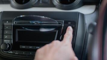 A person is pointing at the CD button in a car. The person is wearing glasses and is looking at the CD player photo