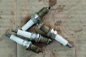 Used spark plugs. The spark plugs are extremely old. Four of them are lined up for a 4 cylinder engine. On the stained brown paper. photo
