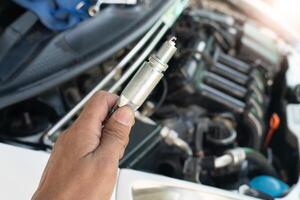 Car mechanic hand holding spark plug to repair car engine in garage. A set of socket wrenches to lock the spark plugs in place. ready to be put back into the engine system. photo