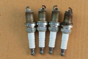 Used spark plugs. The spark plugs are extremely old. Four of them are lined up for a 4 cylinder engine. On old brown paper. photo