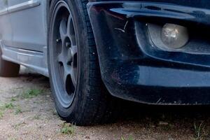 Perspective of front used black car. Can see old style wheels and front bumper with fog lights. Car driving on soil road with green grass at day. photo
