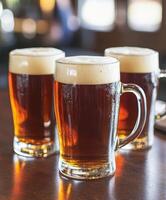 Cold beers with frothy tops on a wooden bar table during happy hour photo