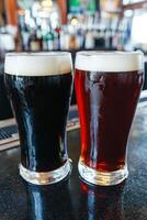 Two glasses of dark and light beer on bar counter in lively pub photo
