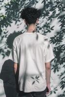 Young man with curly hair standing against a wall with shadows in daylight photo