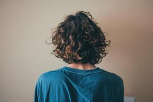 Young man with curly hair facing a wall in a casual indoor setting photo