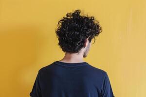 Young man with curly hair stands against a bright yellow wall photo