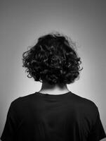 Young man with curly hair standing against a plain background photo