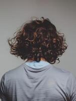 Young man with curly hair poses against a neutral backdrop indoors photo