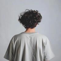 Young man with curly hair poses against a plain background indoors photo