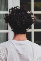 Young man with curly hair standing by a window on a sunny day photo
