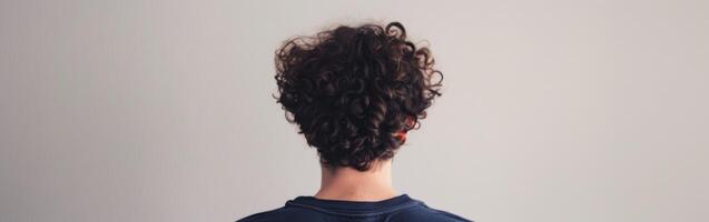 Young man with curly hair standing against a plain wall indoors photo