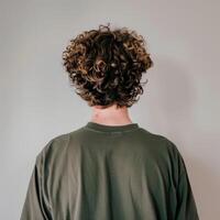 joven hombre con Rizado pelo frente a un llanura pared en interior ajuste foto