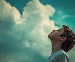 High school boy gazing up at fluffy clouds in a clear blue sky photo