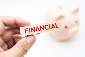 Text FINANCIAL on wooden block with piggy bank on the background. Financial and business concept. photo