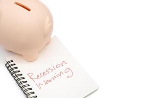 Hand writing Recession Warning on notebook with piggy bank. Global economic crisis. Recession business and stock crisis concept. photo