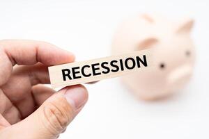 Text RECESSION on wooden block with piggy bank on the background. Financial and business concept. photo