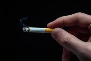 Close-up of a hand holding a lit cigarette on a black background photo