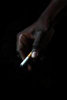 Close-up of a hand holding a cigarette against a black background photo