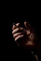 Close-up of a hand holding a cigarette against a black background photo