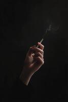 Close-up of a hand holding a cigarette with smoke on black background photo