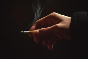 Close-up of a hand holding a cigarette with smoke on a dark background photo