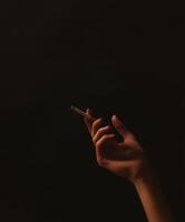 Close-up of a hand holding a cigarette against a black background photo