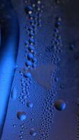 A drop of water on a glass close-up macro with sparkling bokeh on blue blurred background. Abstract drop water. Raindrop slide down the window glass, forming abstract figure video