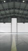 Roller shutter door and concrete floor inside factory building for industrial background. Airplane in front of half opened door to hangar. The open door of the hangar. Mechanic opening the door video