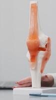 Orthopedic specialist analyzes imaging results in a modern office, using a laptop and knee joint model for detailed assessment. Showcases advanced orthopedic diagnostics and consultation.Vertical shot video