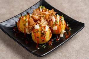 Takoyaki is a ball-shaped Japanese snack made of a wheat flour-based batter and cooked in a special molded pan photo