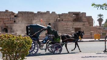 EGYPT, KARNAK - MARCH 01, 2019 a cart with a horse for walking with tourists against the backdrop of the temple complex in Karnak, Egypt photo