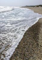 Wide sandy beach, waves with white foam roll on the shore photo
