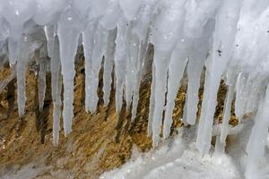 Ice icicles on a yellow stone, the Black Sea froze, ice covered coastal stones. Climate change, harsh winter photo