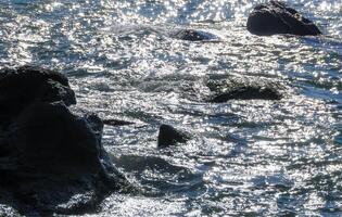 Bright reflections on the water on a sunny day among the coastal rocks near the Black Sea coast photo