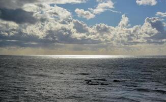 The sun's rays break through thick clouds over the Pacific Ocean, a sunspot is all over the water. photo