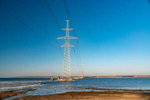 High-voltage power line against the background of the blue sky above the water of the lake photo