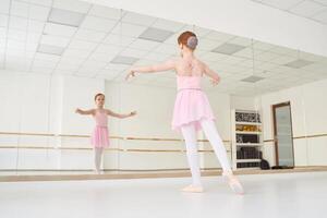 Young ballet girl at studio lesson. Training performance. Stretching exercise pose. Ballerina practice balance technique. Classical elegance fitness. Dancing costume. Pink dress, skirt photo