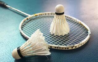 Cream white badminton shuttlecock and racket with neon light shading on dark floor in indoor badminton court, copy space, soft and selective focus. photo