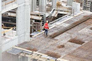 Aerial view of busy industrial under construction site workers working with cranes and excavators. Top view of precast concrete slap floor full of steel. Development high rise architecture building. photo
