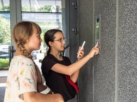 two teenagers getting access to the building by attaching smartphone to intercom. Concept of modern security technologies for access and smart home photo