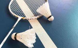 Cream white badminton shuttlecock and racket with neon light shading on dark floor in indoor badminton court, copy space, soft and selective focus. photo